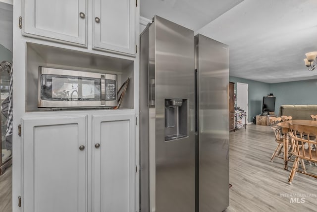 kitchen featuring appliances with stainless steel finishes, an inviting chandelier, open floor plan, white cabinets, and light wood-type flooring