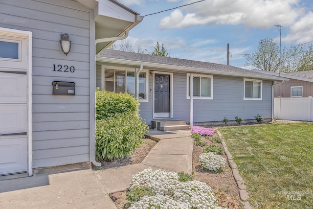 property entrance featuring a yard, a shingled roof, and fence