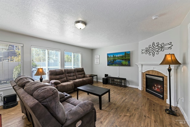 living area featuring baseboards, a textured ceiling, wood finished floors, and a tile fireplace