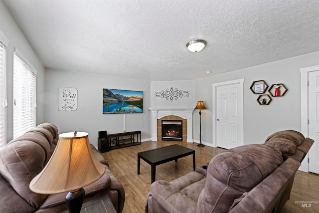 living area with a tiled fireplace, wood finished floors, baseboards, and a textured ceiling