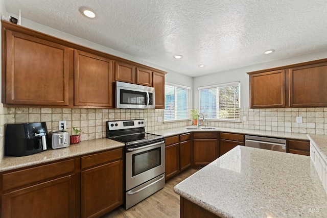 kitchen with a sink, tasteful backsplash, stainless steel appliances, brown cabinetry, and light wood finished floors