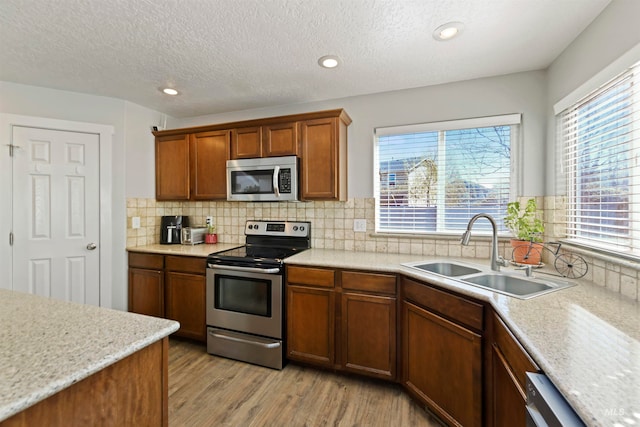 kitchen with a sink, tasteful backsplash, light wood-style floors, appliances with stainless steel finishes, and light countertops