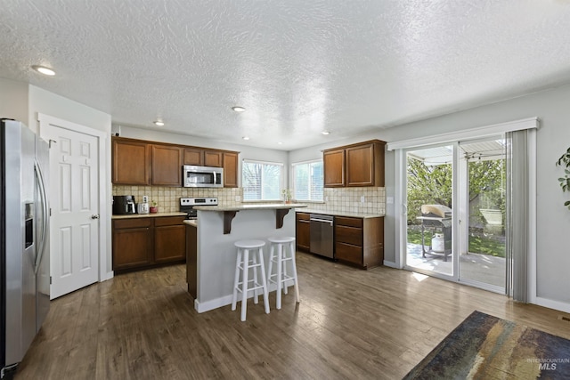 kitchen featuring a kitchen breakfast bar, appliances with stainless steel finishes, dark wood-style floors, and light countertops