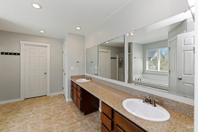 bathroom with a textured ceiling, a garden tub, double vanity, and a sink