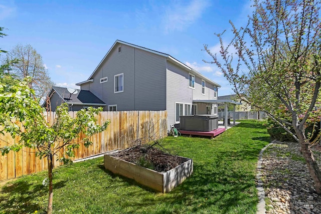 back of property with a yard, a hot tub, and a fenced backyard