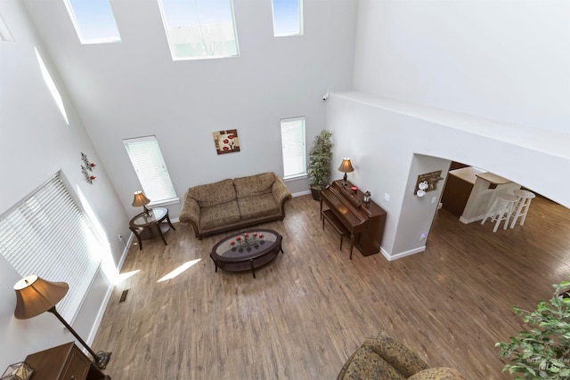 living room with a skylight, baseboards, a high ceiling, and wood finished floors