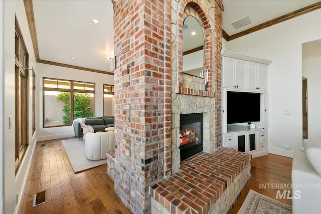 living room featuring brick wall, wood-type flooring, ornamental molding, and a fireplace