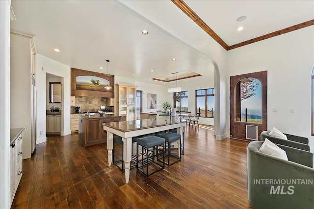 kitchen with dark hardwood / wood-style floors, a kitchen breakfast bar, a center island with sink, crown molding, and pendant lighting