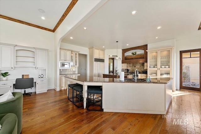 kitchen with a spacious island, dark stone counters, hardwood / wood-style floors, decorative light fixtures, and built in appliances