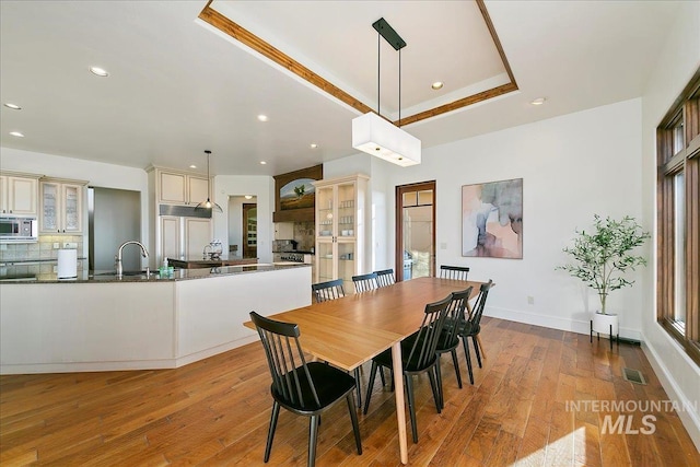 dining room with a tray ceiling, sink, wood-type flooring, and plenty of natural light