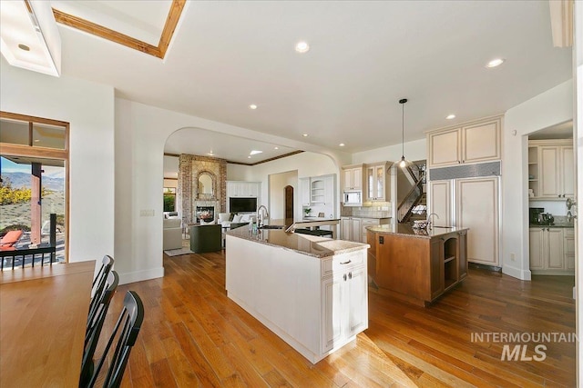 kitchen with decorative light fixtures, a large fireplace, cream cabinets, built in appliances, and light wood-type flooring