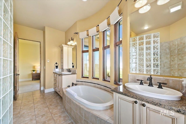 bathroom with a relaxing tiled bath, a healthy amount of sunlight, oversized vanity, and dual sinks