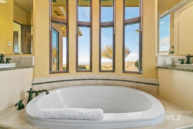 bathroom with a wealth of natural light, vanity, and a relaxing tiled bath