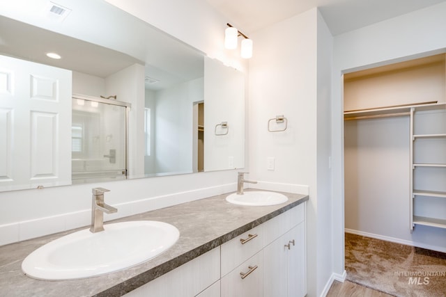 bathroom with a shower stall, a sink, a spacious closet, and double vanity
