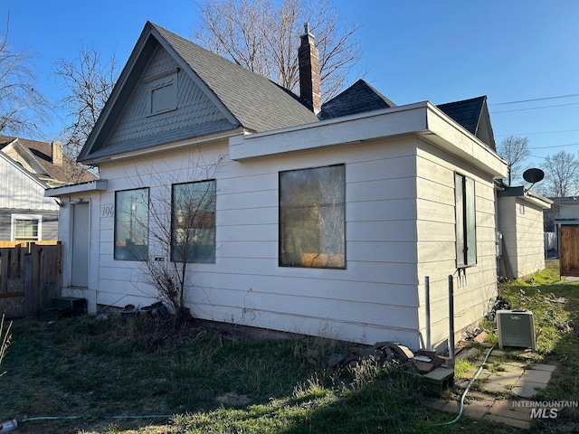 view of side of home with roof with shingles, fence, and a chimney