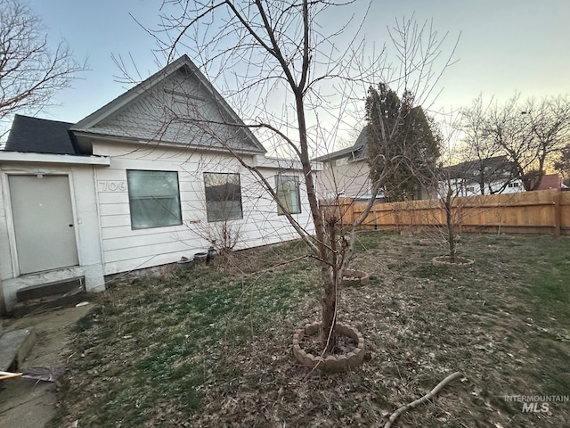 rear view of house with entry steps, fence, and roof with shingles