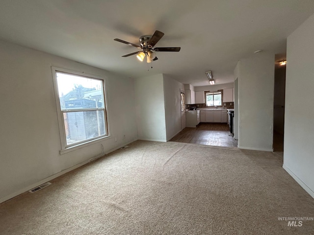 unfurnished living room featuring ceiling fan, carpet flooring, visible vents, and baseboards