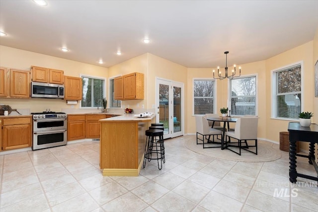 kitchen featuring a kitchen breakfast bar, stainless steel appliances, an inviting chandelier, a peninsula, and light countertops