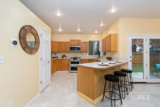 kitchen with a breakfast bar area, a peninsula, light tile patterned flooring, light countertops, and appliances with stainless steel finishes