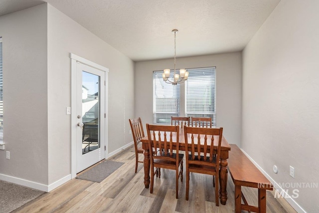 dining space featuring an inviting chandelier, a textured ceiling, baseboards, and light wood-style floors