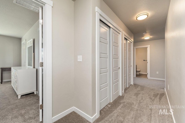 corridor featuring carpet floors, visible vents, a textured ceiling, and baseboards