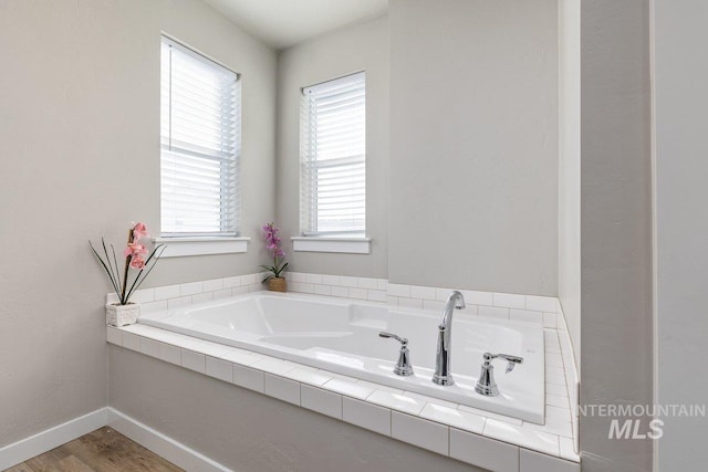 full bathroom with wood finished floors, a garden tub, and baseboards