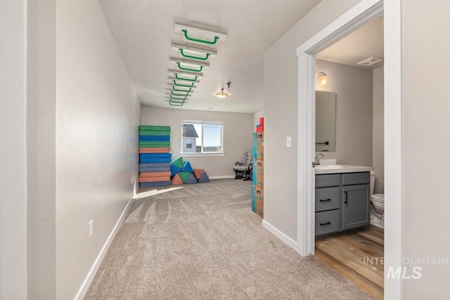 game room with a textured ceiling, carpet flooring, a sink, visible vents, and baseboards