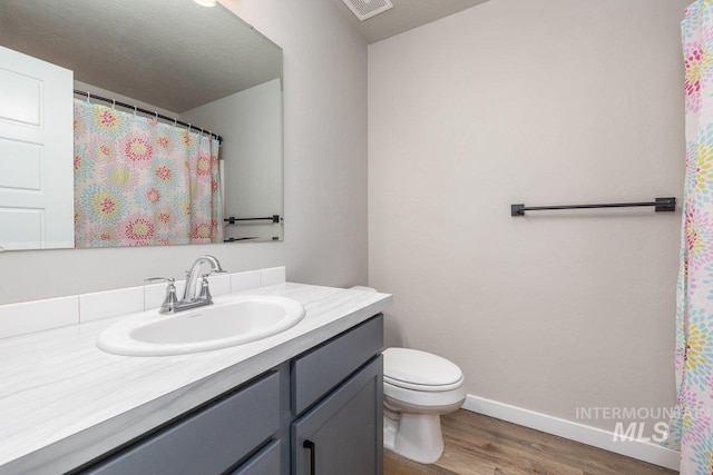 full bathroom with visible vents, toilet, vanity, wood finished floors, and baseboards