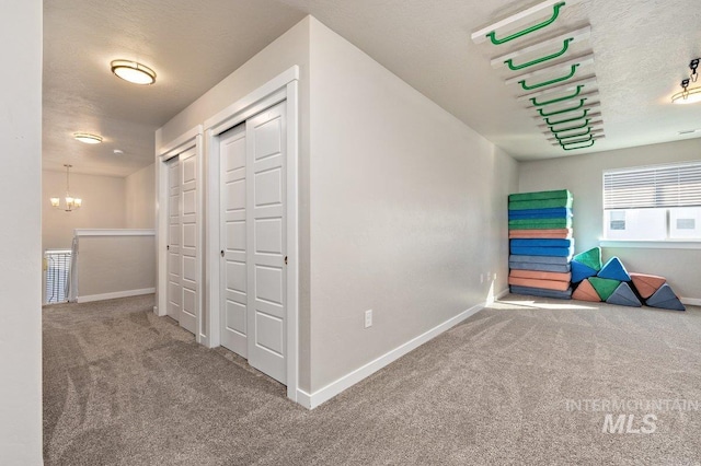 hallway featuring a textured ceiling, carpet floors, baseboards, and a notable chandelier