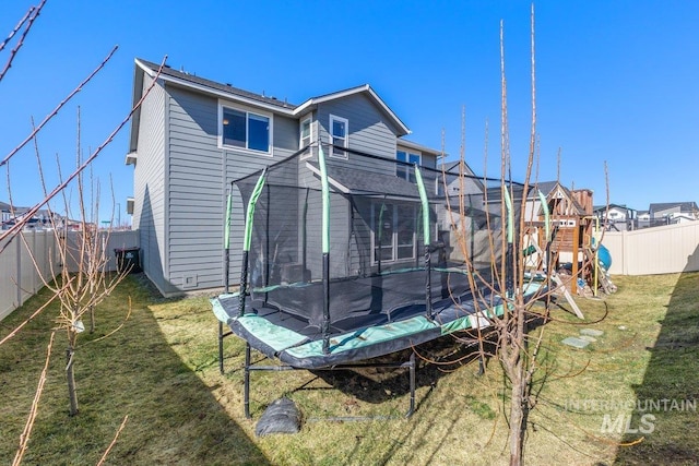 rear view of property featuring a trampoline, a playground, a lawn, and a fenced backyard