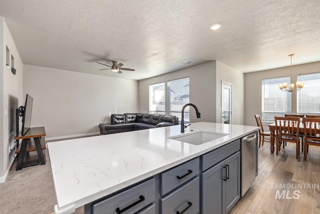 kitchen featuring dishwasher, a kitchen island with sink, gray cabinets, and a sink