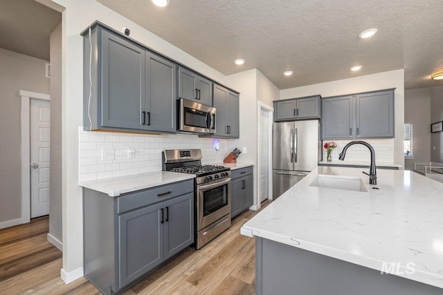 kitchen with gray cabinets, appliances with stainless steel finishes, light wood-style floors, a sink, and light stone countertops