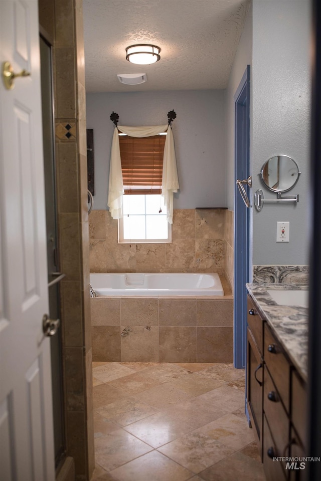 bathroom featuring vanity, a relaxing tiled tub, and a textured ceiling