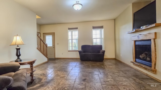 interior space with a glass covered fireplace, stairs, baseboards, and stone tile flooring