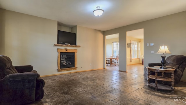 living area featuring baseboards, stone tile floors, and a glass covered fireplace
