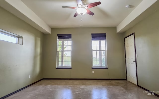 empty room with a wealth of natural light, finished concrete flooring, and a ceiling fan