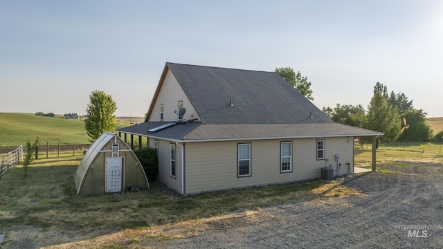 back of property featuring an outdoor structure, fence, central AC, and a shingled roof