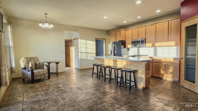 kitchen featuring fridge with ice dispenser, light countertops, a kitchen island with sink, stainless steel microwave, and recessed lighting