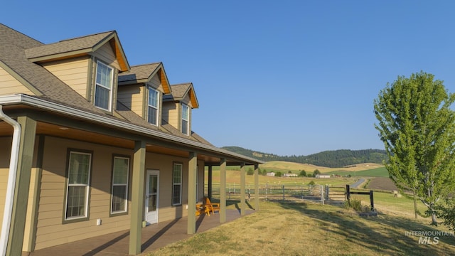 view of home's exterior with a mountain view, a shingled roof, a lawn, fence, and a patio