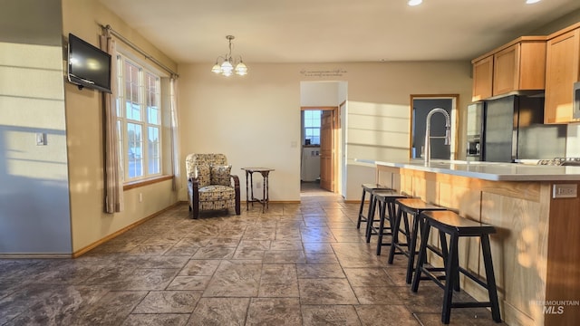 kitchen with baseboards, black refrigerator with ice dispenser, an inviting chandelier, stone tile flooring, and a breakfast bar