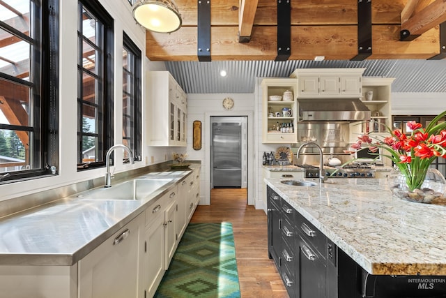 kitchen with stainless steel counters, built in refrigerator, a sink, open shelves, and dark cabinets