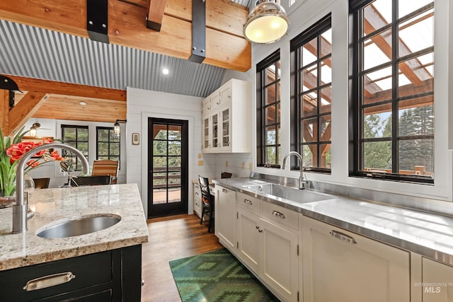 kitchen with a sink, stainless steel countertops, dark wood-style flooring, white cabinets, and beam ceiling