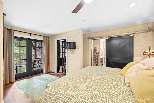 bedroom with access to exterior, french doors, a barn door, wood finished floors, and wood walls