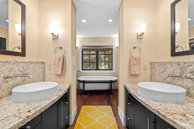 bathroom featuring decorative backsplash, wood finished floors, a freestanding tub, two vanities, and tile walls