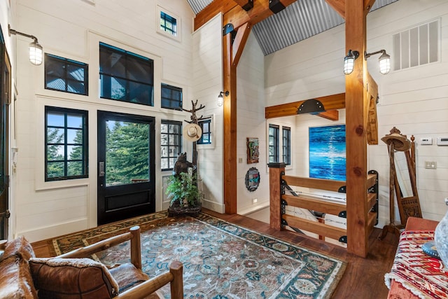 foyer entrance featuring wood finished floors, wood walls, healthy amount of natural light, a towering ceiling, and baseboards