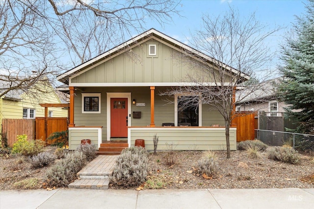 bungalow with board and batten siding, covered porch, and fence