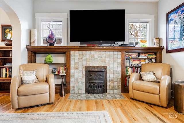 living area with a tiled fireplace, plenty of natural light, wood finished floors, and arched walkways