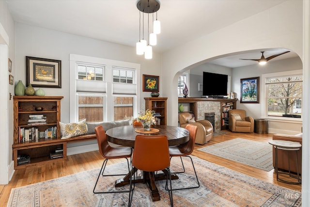 dining area with a tiled fireplace, wood finished floors, arched walkways, baseboards, and ceiling fan