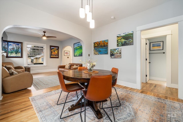 dining room with light wood-type flooring, arched walkways, baseboards, and a ceiling fan