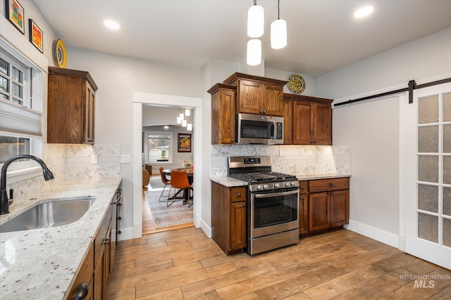 kitchen featuring light wood-style flooring, appliances with stainless steel finishes, a barn door, and a sink